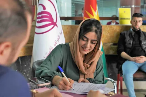 image of a person signing a contract with another person sitting and waiting in the background