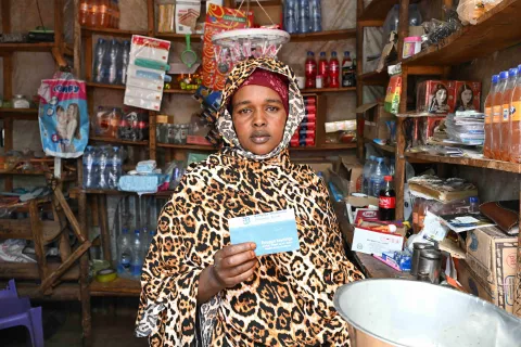 Image of a lady sitting in front of a local shop with a document from a bank in hand